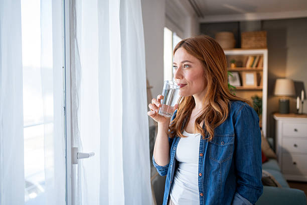 istock Serene woman drinking water by the window in morning light 2216693637