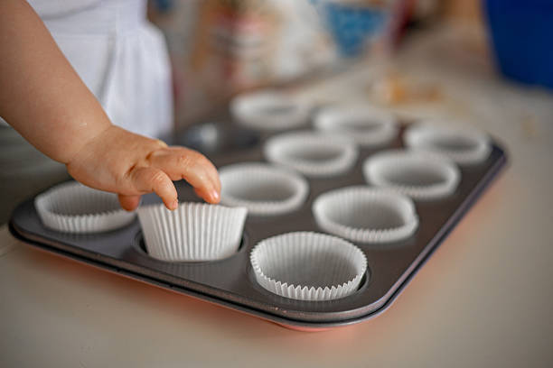 Small child’s hands carefully arranging cupcake liners in a muffin pan, capturing a sweet and detailed moment of early kitchen fun.