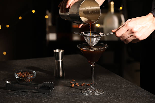 istock Bartender making delicious espresso martini at dark table against blurred lights, closeup 2216694446