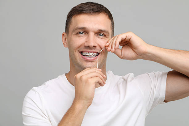 istock Smiling man with braces cleaning teeth using dental floss on grey background 2216695805