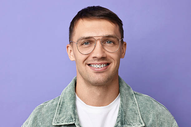 istock Smiling man with dental braces on violet background 2216695827