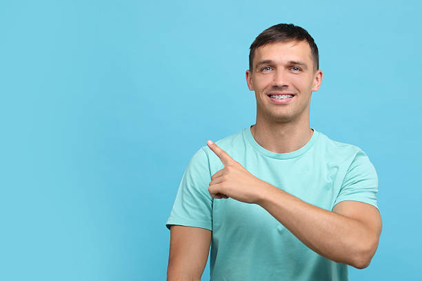 istock Smiling man with dental braces pointing at something on light blue background. Space for text 2216696123