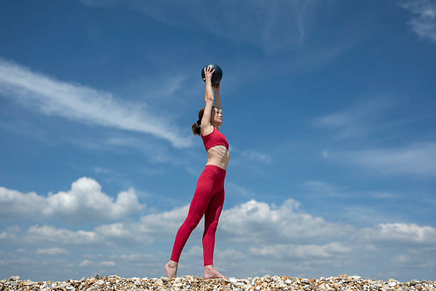 Woman Exercising Outdoors Holding Medicine Ball Under Clear Sky