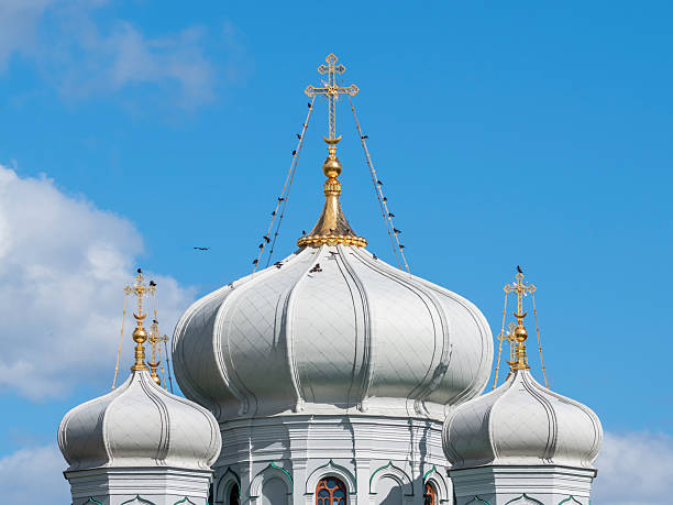 Golden crosses on white domes on the Pavlovsk Cathedral in Gatchina. Jackdaws are sitting on the domes of the cathedral.
