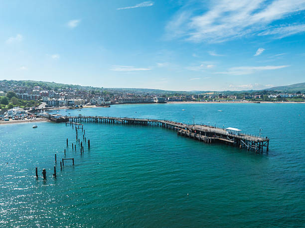 Swanage pier reaching out into the turquoise waters of the english channel, with the town and coastline in the background on a sunny summer day
