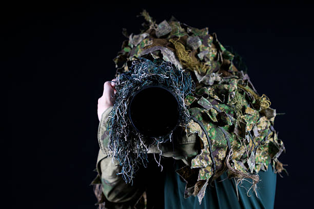 A person is wearing a camouflage jacket and holding a camera. The person is taking a picture of something, but the camera is obscured by the foliage on the jacket. Concept of adventure and exploration