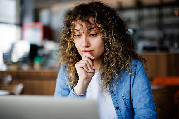 Young thoughtful woman working on her laptop in a cafe