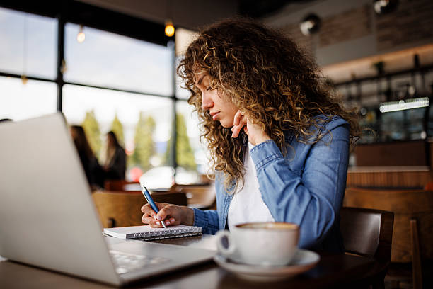 istock Female student taking notes and studying online in a cozy cafe environment 2216717695