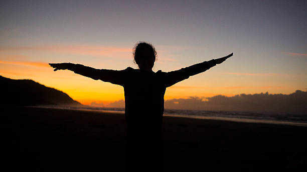 Silhouette Stretching on Beach at Sunrise with Orange Sky