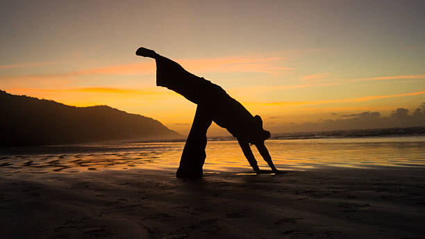 istock Silhouette Stretching on Beach at Sunrise with Orange Sky 2216720119