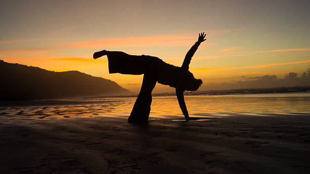 Silhouette Stretching on Beach at Sunrise with Orange Sky