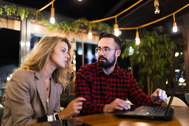istock Two colleagues collaborate over a laptop in a cozy cafe setting, discussing ideas and reviewing work. The warm lighting and greenery create a relaxed atmosphere for productive business conversation. 2216720797