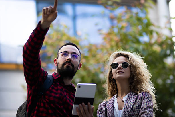 istock Young man and woman exploring urban streets using a digital tablet and sharing ideas, while pointing upwards to navigate their route on a sunny day, wearing casual outdoor attire. 2216720857