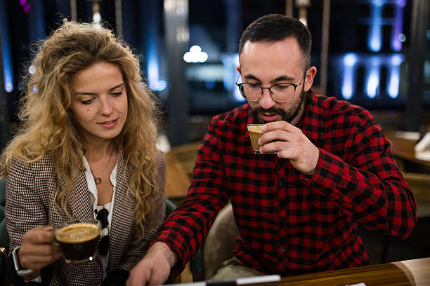 Young couple enjoying coffee together at a cozy cafe, sharing a warm and intimate moment. They are seated indoors, engaging in conversation, with a relaxed and friendly atmosphere reflecting friendship and connection.
