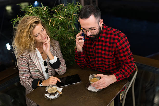 A man and woman in a cafe setting enjoying coffee. The man is on the phone while the woman listens attentively, creating a relaxed and engaging atmosphere.