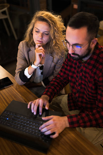 istock Two colleagues engage in a thoughtful discussion while working on a laptop in a cozy, dimly lit cafÃ© setting, highlighting collaboration and teamwork in a professional atmosphere. 2216720916