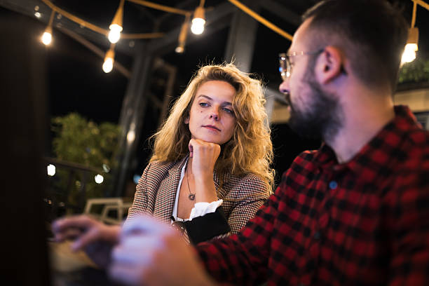 istock Young professionals engaging in a focused conversation at an outdoor cafe during nighttime, illuminated by decorative lights, creating an intimate atmosphere and highlighting the woman's contemplative expression 2216720923