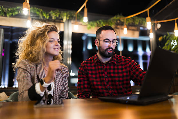 istock Two colleagues collaborating in a modern office space during the evening, discussing ideas and sharing insights at a laptop while sitting at a wooden table, surrounded by stylish decor and ambient lighting. 2216720939
