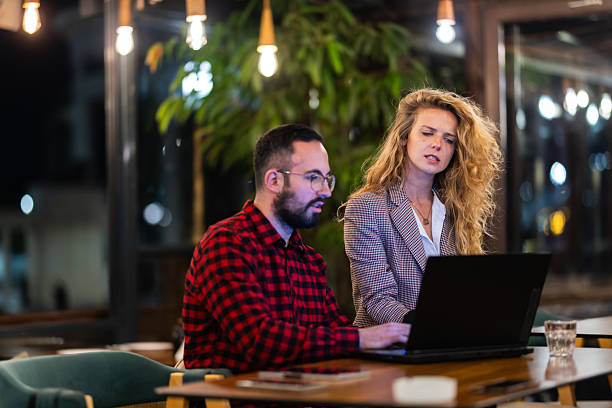 istock Two professionals engaged in a collaborative discussion at a modern workspace, illuminated by stylish hanging lights and surrounded by lush greenery, focusing intently on a laptop screen to share ideas and insights. 2216720944