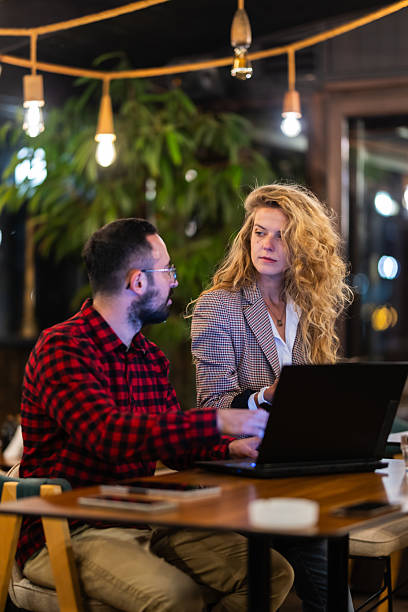istock Two colleagues collaborating on a project in a cozy cafe, engaged in a discussion over a laptop under warm ambient lighting, creating a productive and relaxed workplace atmosphere. 2216720955