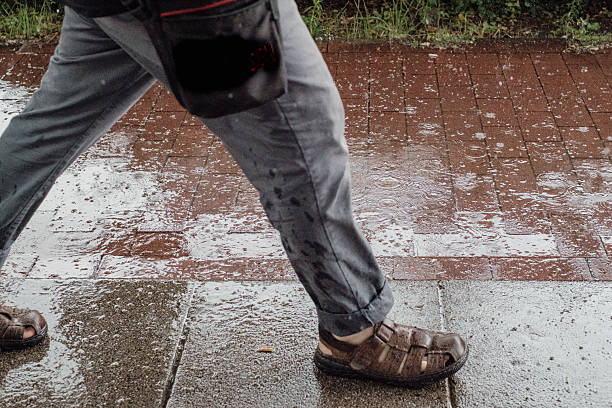 istock a man wearing sandals walks on a sidewalk through heavy rain 2216722239