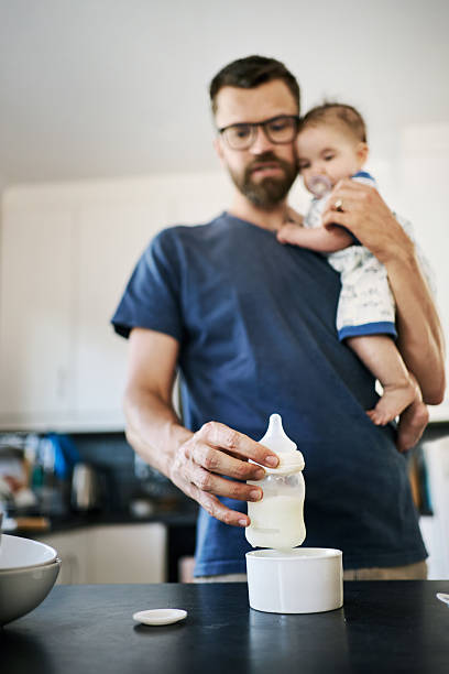 istock Father warming up baby bottle while holding his baby 2216724772