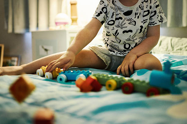 Young child sits on their bed and playing with colorful building blocks at home