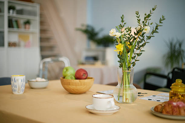 Beautifully set brunch table featuring a vase of fresh flowers, a bowl with fruits, and a coffee mug, all arranged on a neat tablecloth in a cozy dining room setting