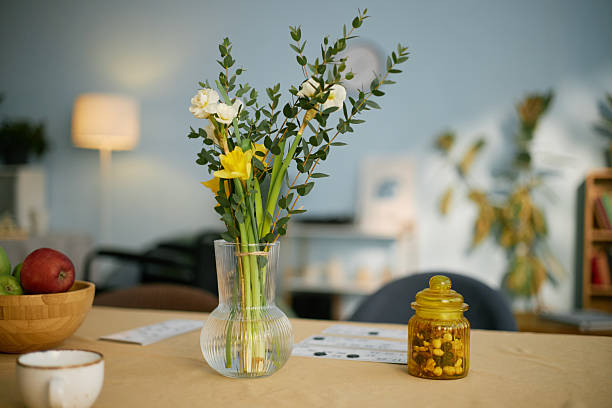 Beautiful yellow and white flowers arranged in a clear glass vase sitting on a table in cozy, well-lit living room setting with soft background lighting