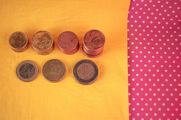 Stacks of various-sized copper coins sit on a light orange surface, with some scattered coins around them. The coins are arranged from shortest to tallest, indicating an increase in quantity or value. The warm hues of the background provide a consistent tone, enhancing the metallic shine of the coins. The setup suggests concepts related to finance, savings, or economic growth.