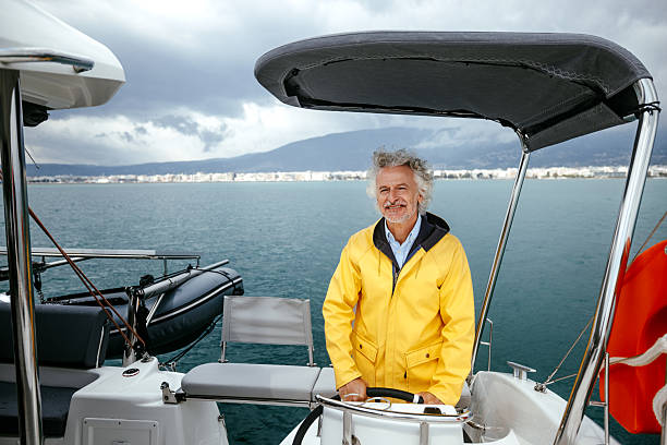 A senior boat captain wearing yellow raincoat steering a catamaran