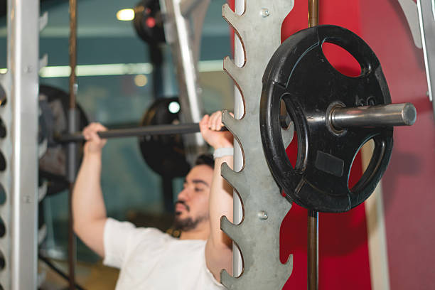 A man doing smith machine shoulder press exercise at gym, fitness center