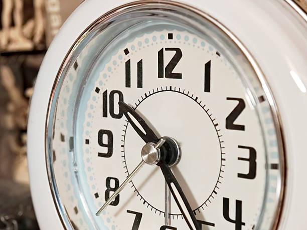 istock Vintage analog clock close up with bold black numbers and white frame, retro timepiece from eastern european block of flats apartment interior, small old-fashioned desk clock showing time 2216750048