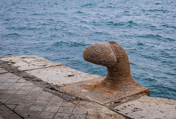 Old, rusty and worn bollard on the dock. Sea in the background.