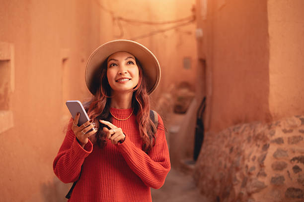 istock Young woman tourist wearing hat and red sweater using mobile phone app for navigation while exploring ancient city 2216763188
