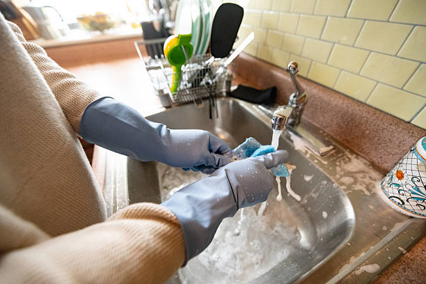 This is a photograph of a Hispanic Man in his 30s wearing rubber gloves to wash dishes at home.