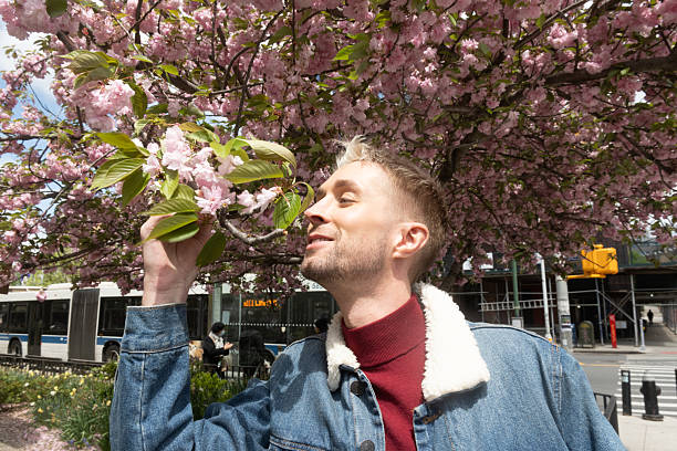 This is a lifestyle photograph of a gay man stopping to admire flowers outdoors on a spring day in New York City.