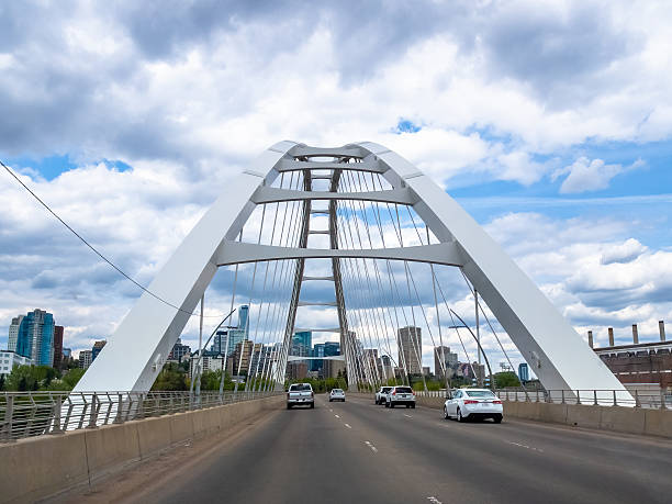 Edmonton, Alberta, Canada. May 21, 2025. The Walterdale Bridge elegantly spans the North Saskatchewan River, its white arches framing the Edmonton skyline against a cloudy sky.