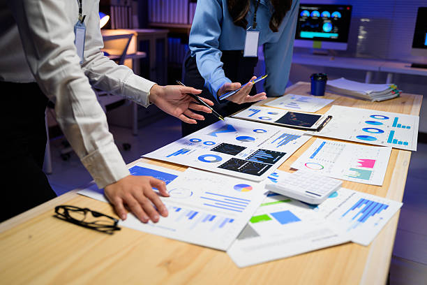 istock Two professionals analyzing financial data and charts on a desk in a modern office. Papers and digital devices display various graphs and statistics 2216772892