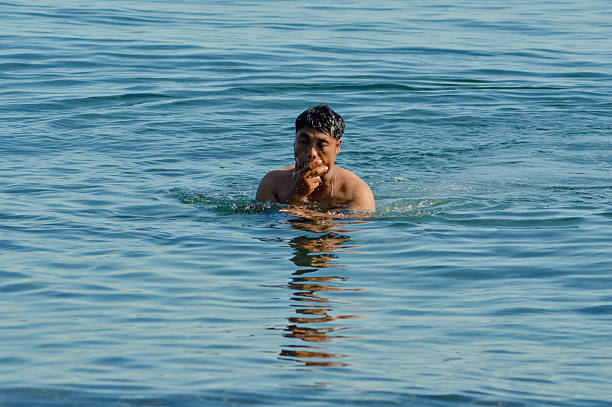After swimming, the father wipes his face as he stands in the shallow sea near the beach.