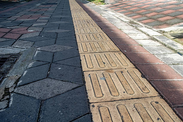 istock Tactile paving guides visually impaired pedestrians on a sidewalk, bordered by dark hexagonal and reddish rectangular bricks. Essential for urban accessibility and public infrastructure 2216783225