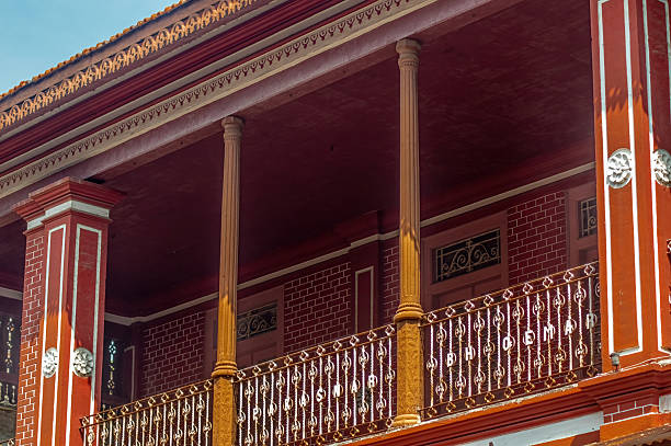 Ornate red building facade with a traditional balcony, featuring detailed railings, columns, and brickwork, showcasing rich historical architecture