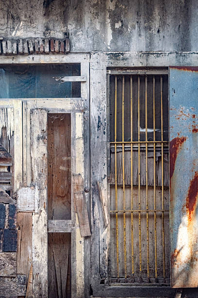 A severely weathered and distressed wooden door with a rusty metal panel and security bars, showcasing extreme urban decay. for themes of abandonment, grunge, poverty, or historical dilapidation