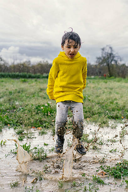 istock Little Boy in Yellow Sweatshirt Jumping Outdoors on a Rainy Day 2216787948