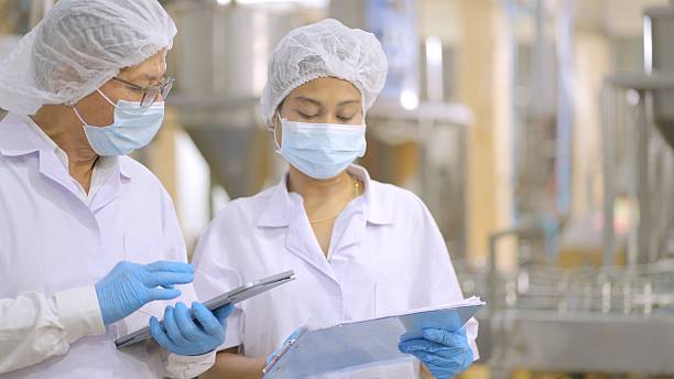 istock Professionals product development team of industrial production is working form discuss the development quality of product. Two food factory employees in white sterile uniforms, discuss about product quantity or raw materials for production line. 2216788295
