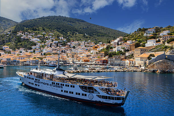 Greece, Hydra  - April 06,  2025 - Passenger cruise ship approaches the picturesque port of Hydra, Greece, with colorful hillside houses and deep blue Aegean Sea.