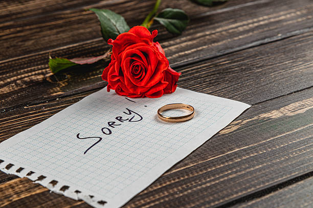 Broken engagement symbolized by a rose, note, and wedding ring on wooden table
