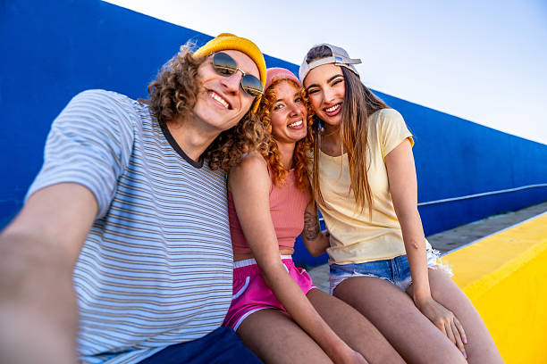 Three cheerful young friends are taking a selfie, enjoying their time together in a colorful urban setting