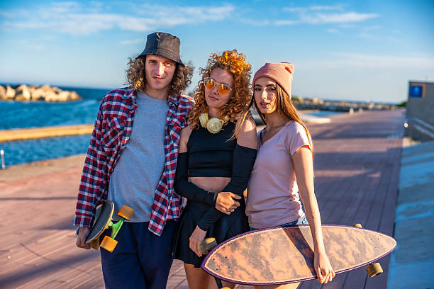 Three young skateboarders posing by the sea, holding their skateboards and enjoying a sunny day filled with laughter and friendship