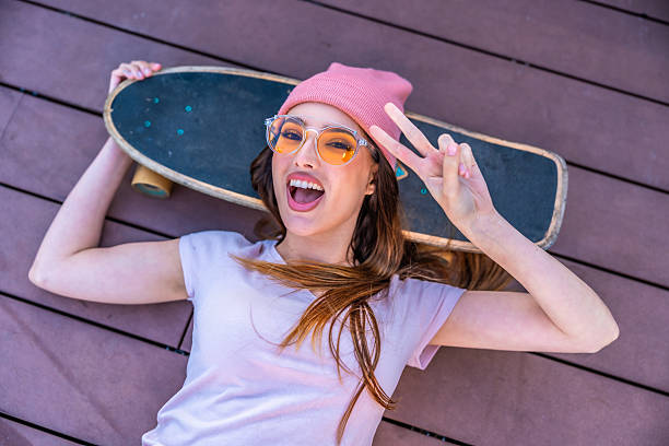 istock Young hipster woman lying on decking with skateboard showing peace sign 2216797632